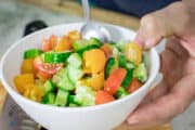 adding the cucumber and tomato to a bowl for adding salt to